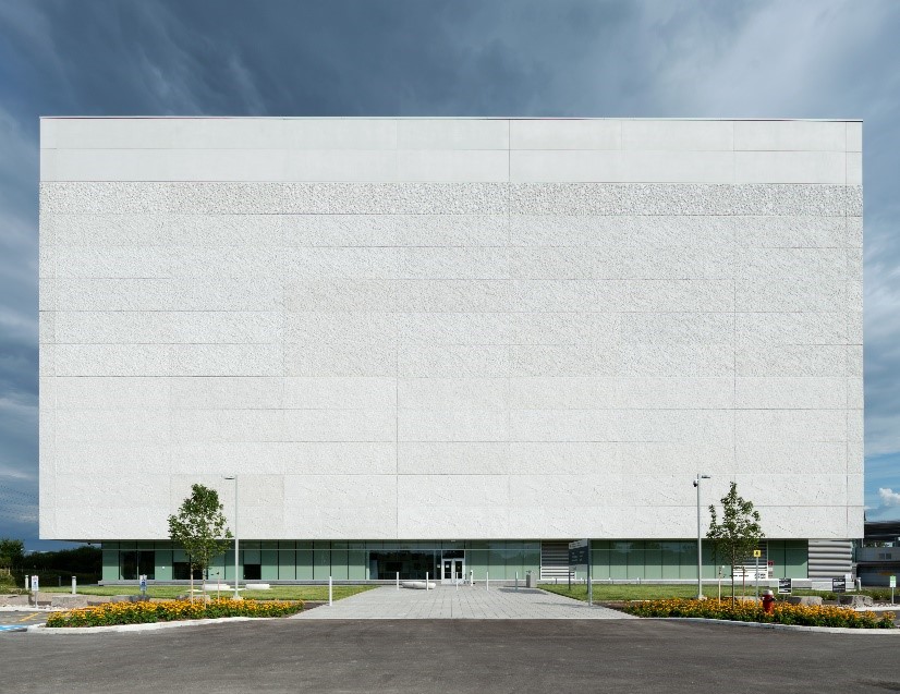 The exterior of the Library & Archives Preservation Centre in Gatineau, Quebec. The building is uniformly square with white horizontal concrete panels decorating the exterior.