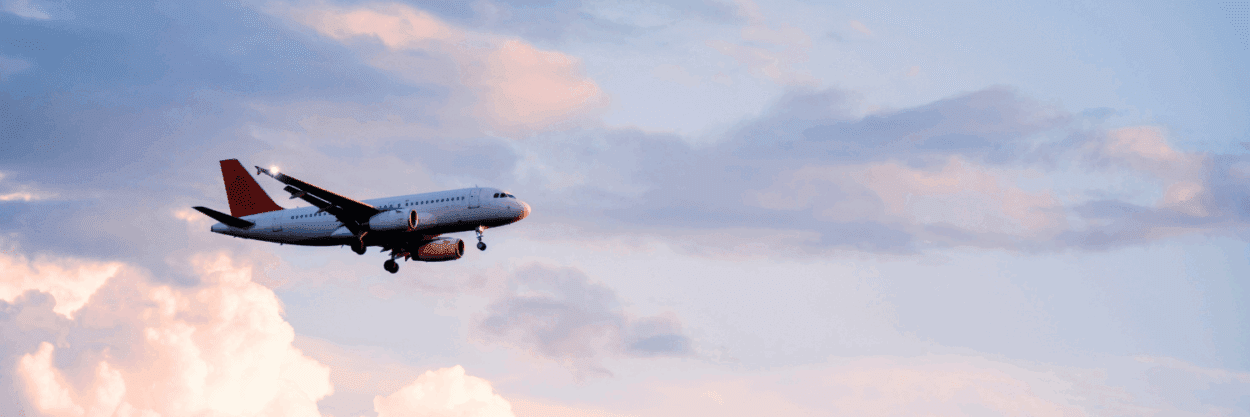 A plane flying in a blue and pink hued sky.