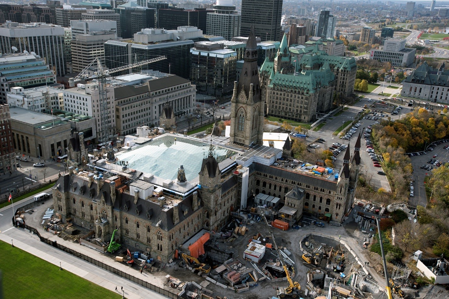 The exterior of West Block taken from above, showing ongoing construction work and the new glass roof of the interim House of Commons Chamber in the center of the existing structure.