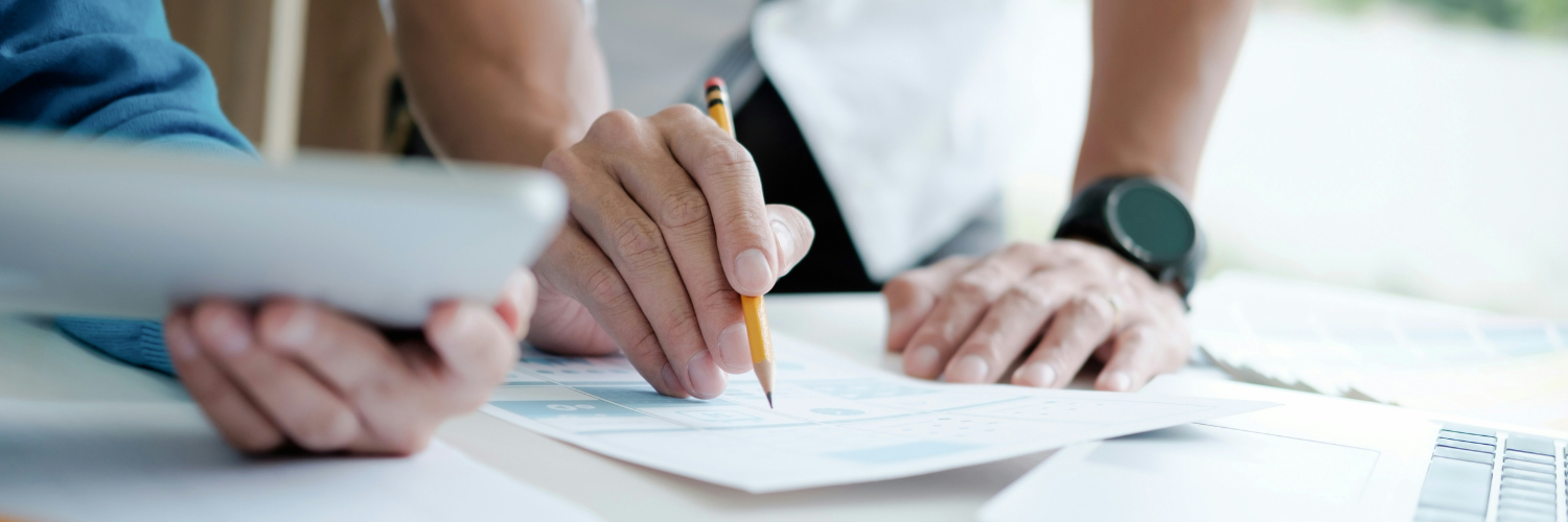 Two men's hands pictured. One holding a pencil indicating something on paper. And the other holding a table towards the first man.