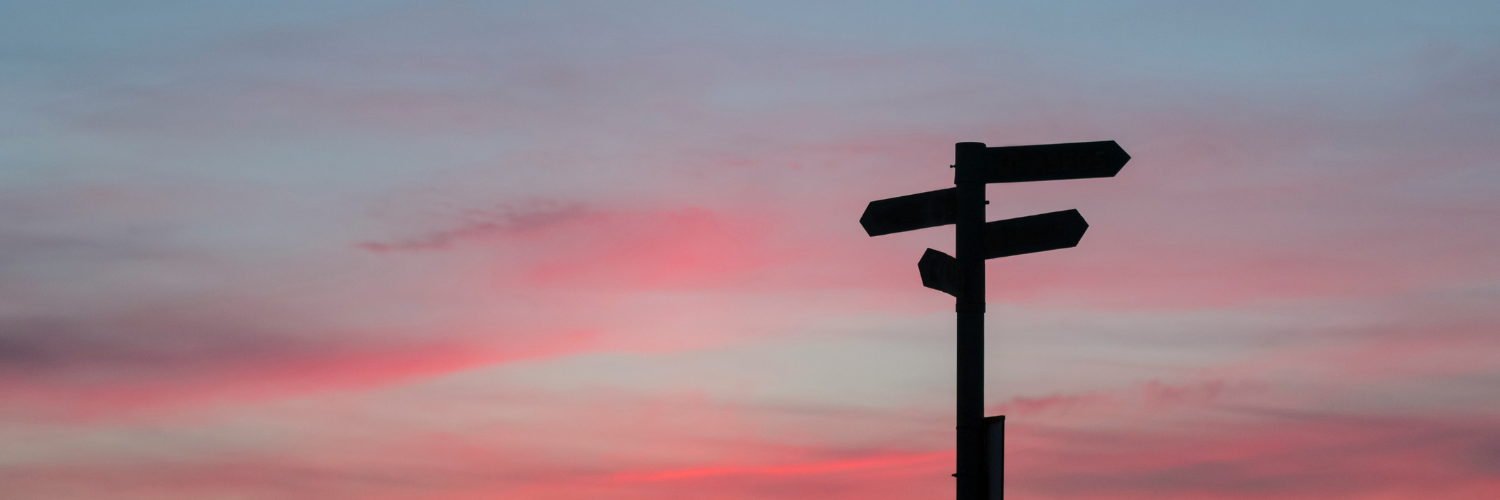 A wayfinding sign backlit by a pink and blue sunset.