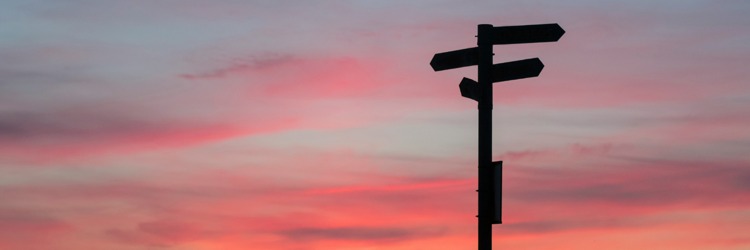 A wayfinding sign backlit by a pink and blue sunset.