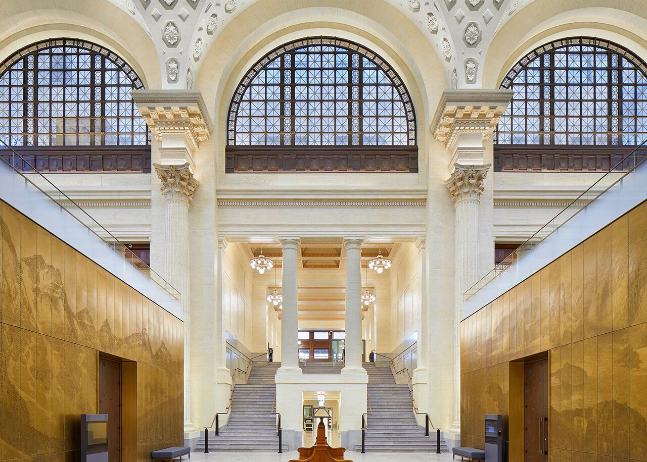 The interior of the Senate of Canada building. Two staircases are pictured with bronze panels on either side showcasing Canadian landscapes.